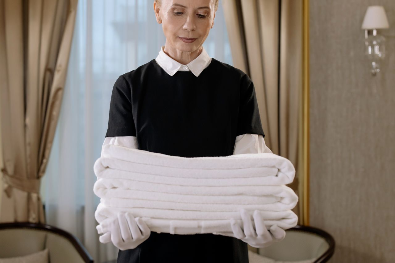 A professional housekeeper is carrying a stack of fresh towels in a luxurious hotel room, highlighting elegance and attentive service.