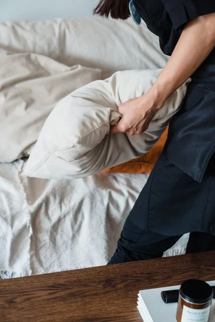 Une femme de chambre professionnelle range des coussins dans une chambre d’hôtel luxueuse, en veillant à maintenir un niveau de service élevé.